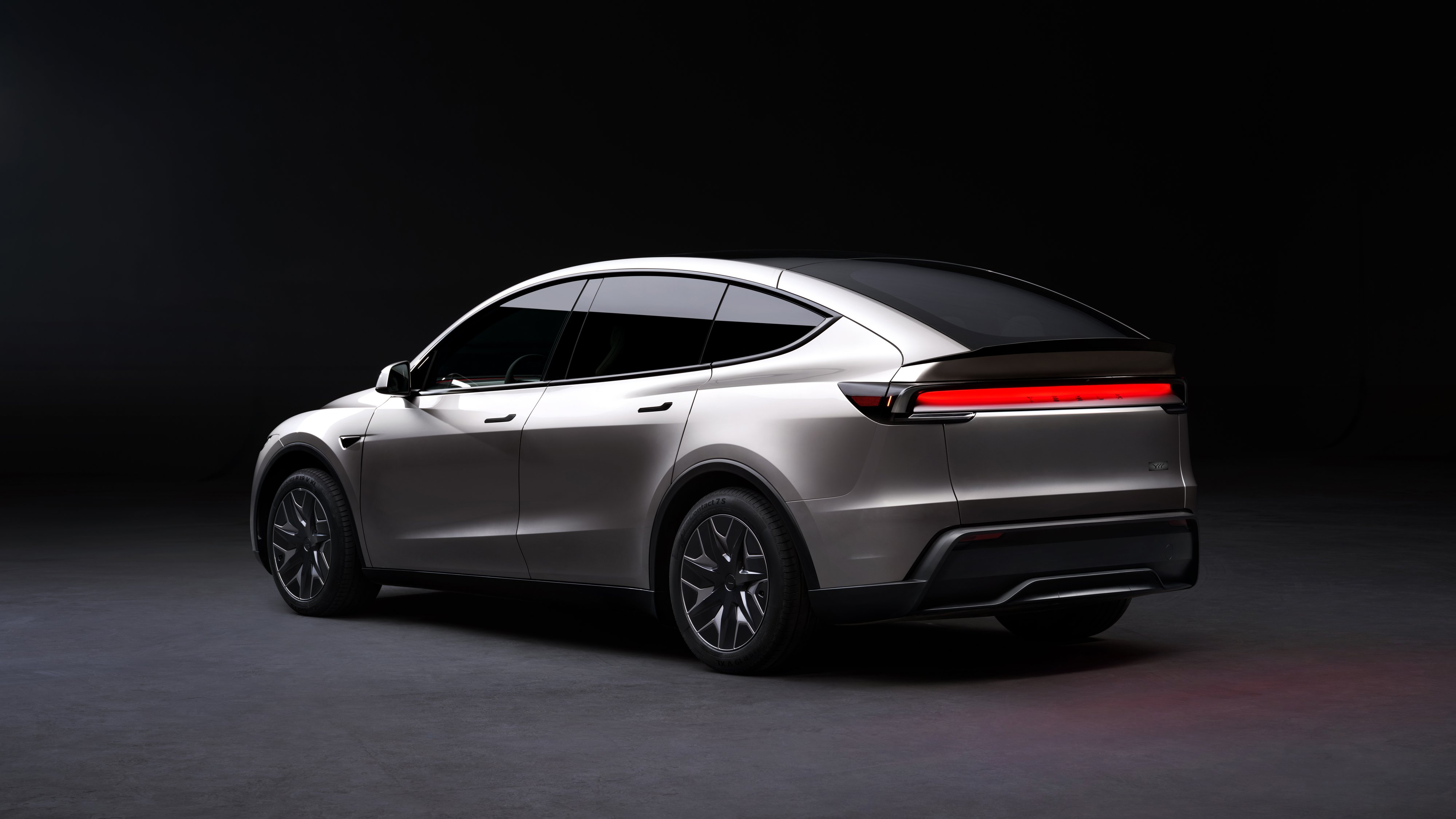 The rear three-quarter view in the studio — the full-width light bar and fastback roofline give the L a cleaner silhouette than the standard Model Y. Image: Tesla